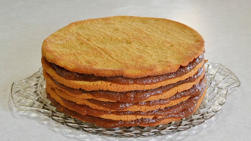 An old-fashioned apple stack cake sits on a glass platter with visible layers of cake and apple filling