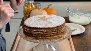An assembled apple stack cake rests on a glass stand, topped with powdered sugar and a star-shaped cutout