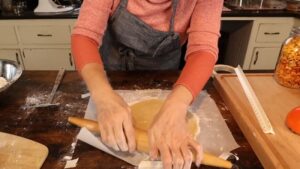 A person rolls out dough on parchment paper using a wooden rolling pin