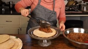 A person spreads apple filling onto a cake layer using a ladle